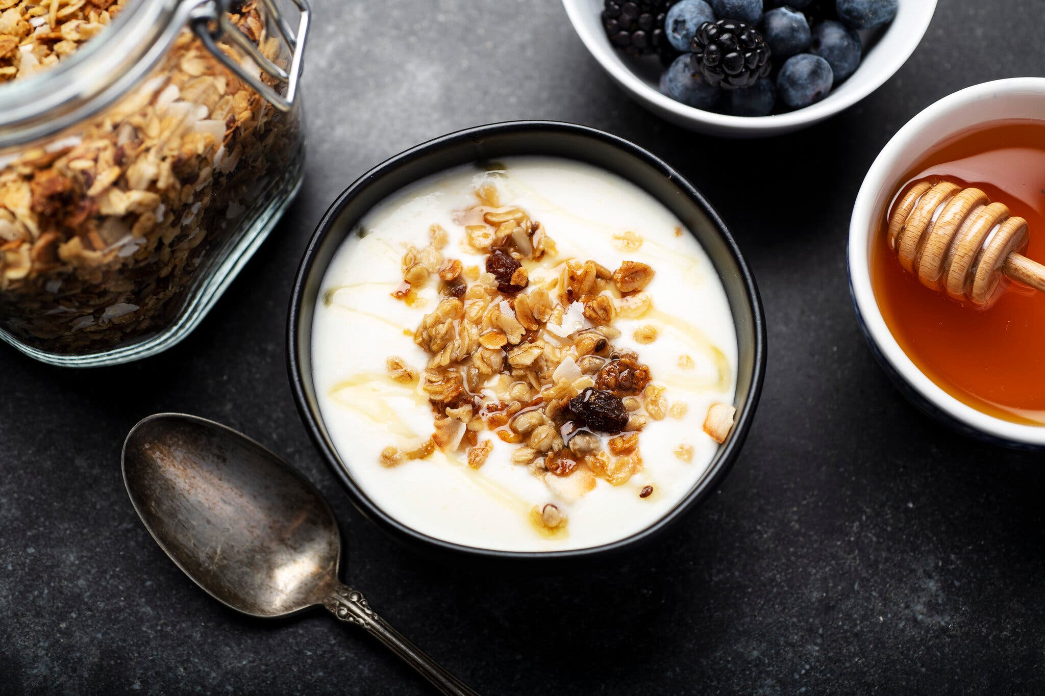 An overhead image of a bowl of yogurt topped with granola and honey. It’s surrounded by other add-ins.