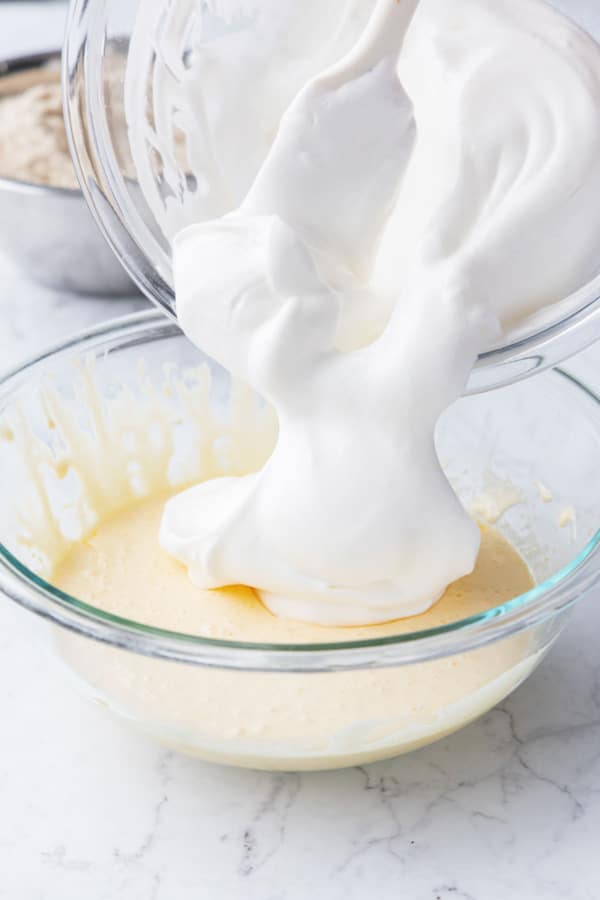 Adding half of whipped egg whites to egg yolk mixture in a mixing bowl.