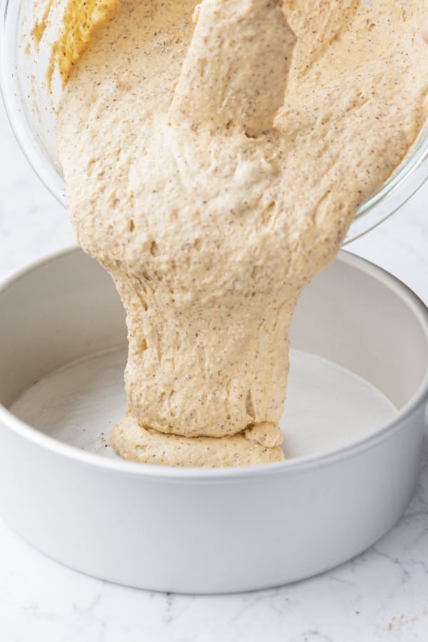 Pouring the finished cake batter into a prepared 9-inch cake pan.