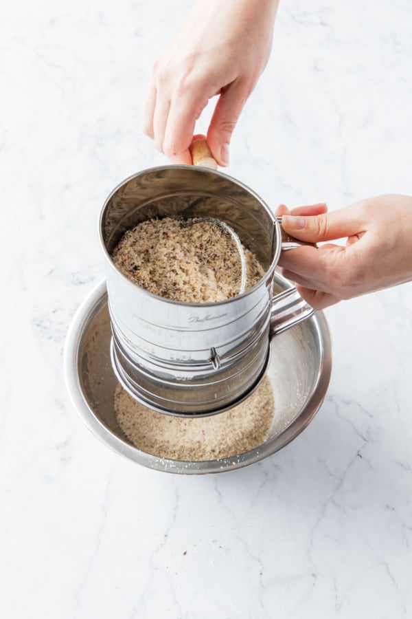 Sifting hazelnut flour through a metal flour sifter.