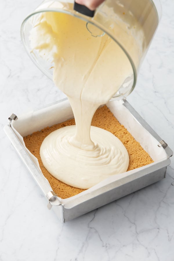 Pouring smooth cheesecake batter into baking pan with pre-baked cookie crust.