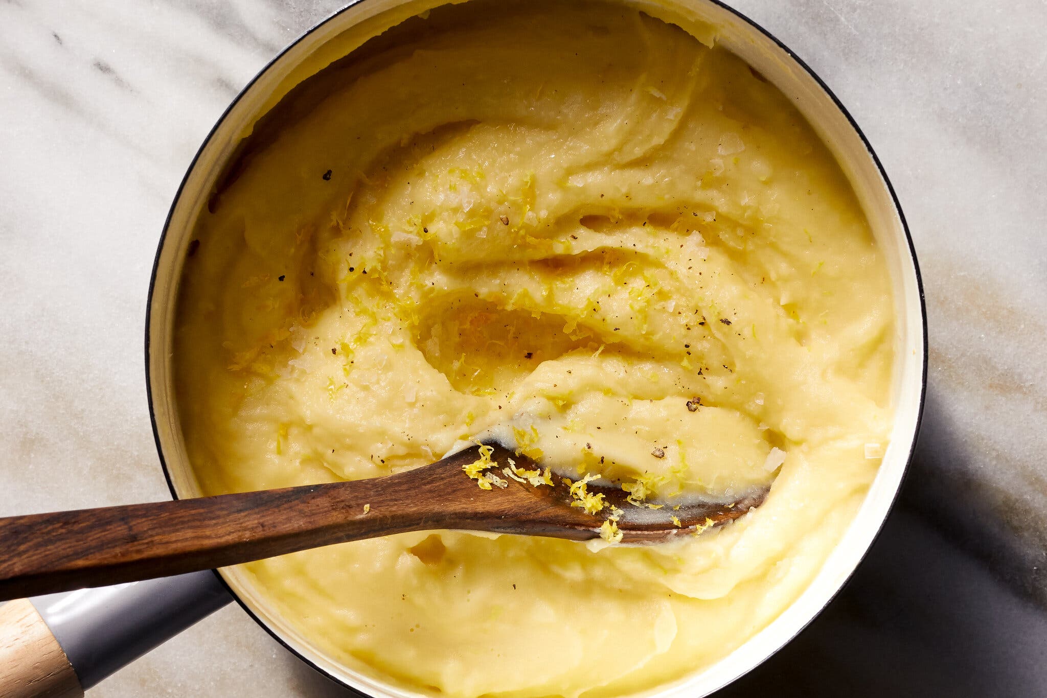 A pot is filled with creamy potatoes stirred by a spoon.