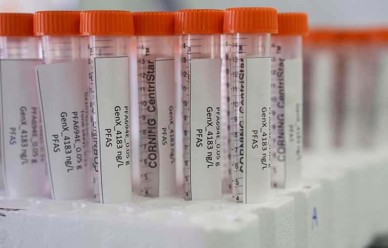 Close-up of row of polystyrene tray with plastic clear vials of corning brand with orange lids with label reporting concentration of pfas.