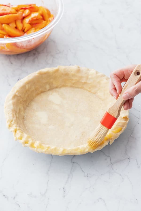 Brushing edge of pie crust with an egg wash.