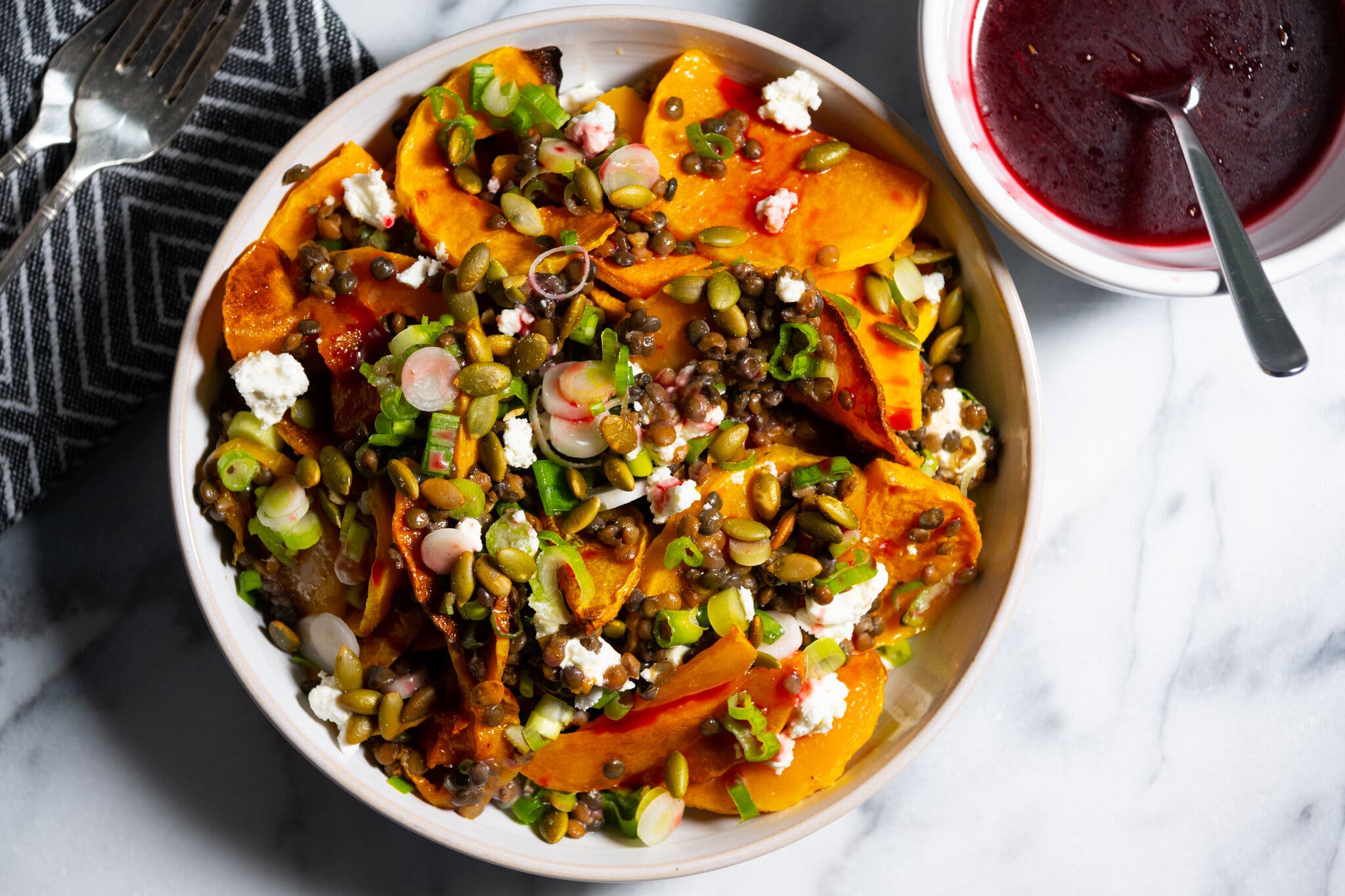 An overhead image of a bowl of butternut squash topped with a mix of pumpkin seeds and scallions.