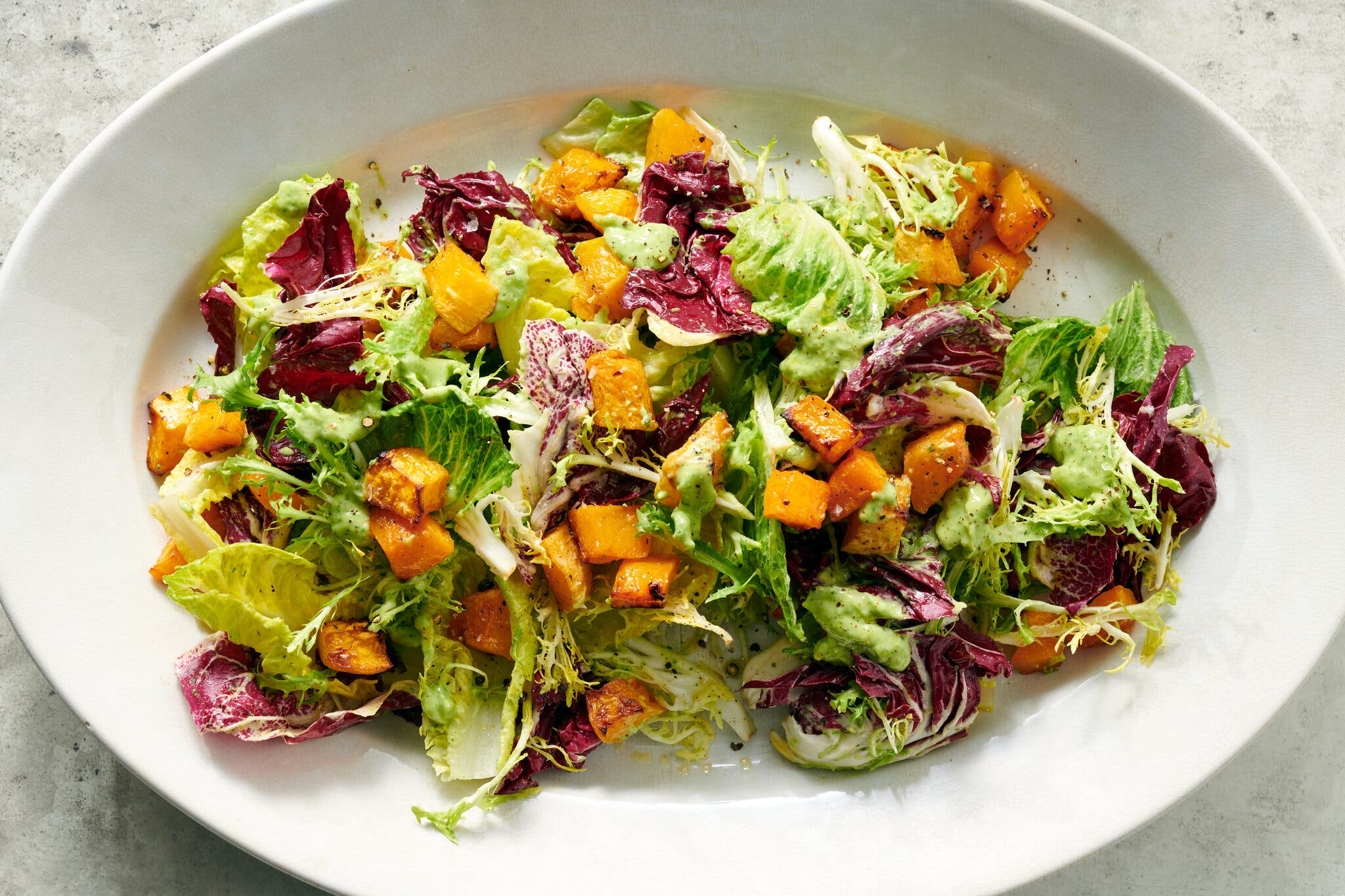 An overhead image of a green salad studded with cubed butternut squash.