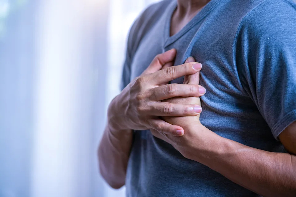 Person in a t-shirt holding their chest with both hands, suggesting discomfort or pain