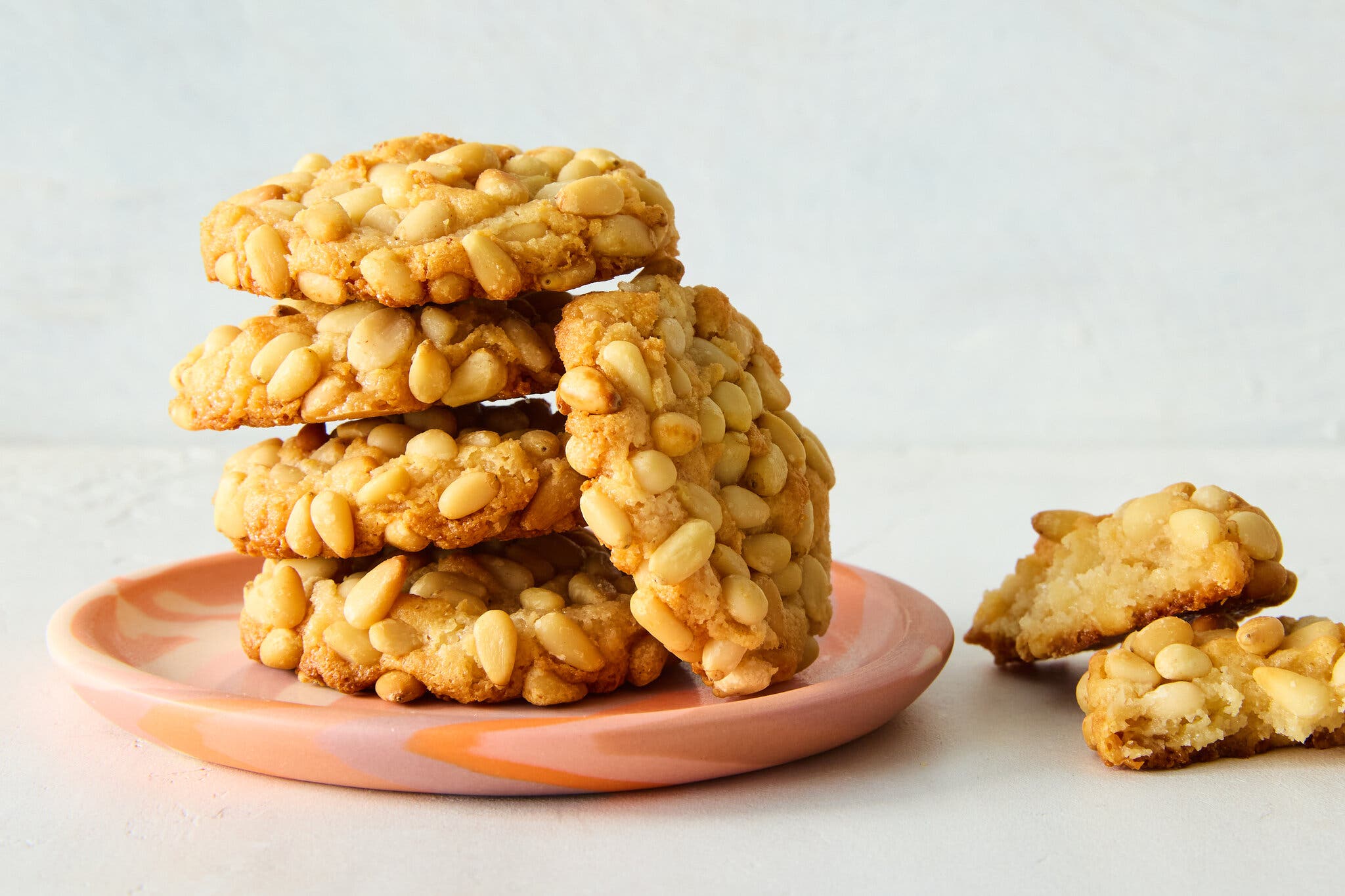 A stack of pignoli cookies sit on a pink plate.