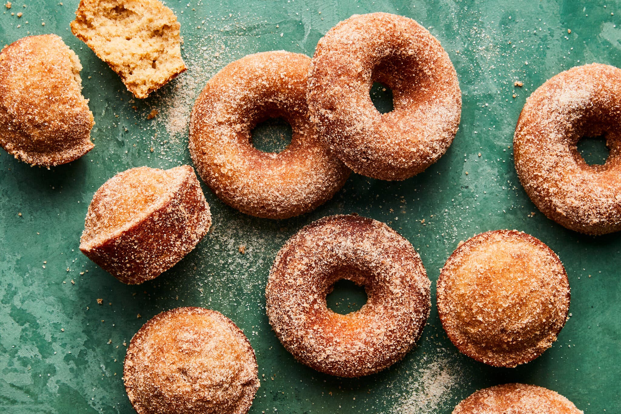 Cinnamon sugar doughnuts and muffins are arranged on a green surface.