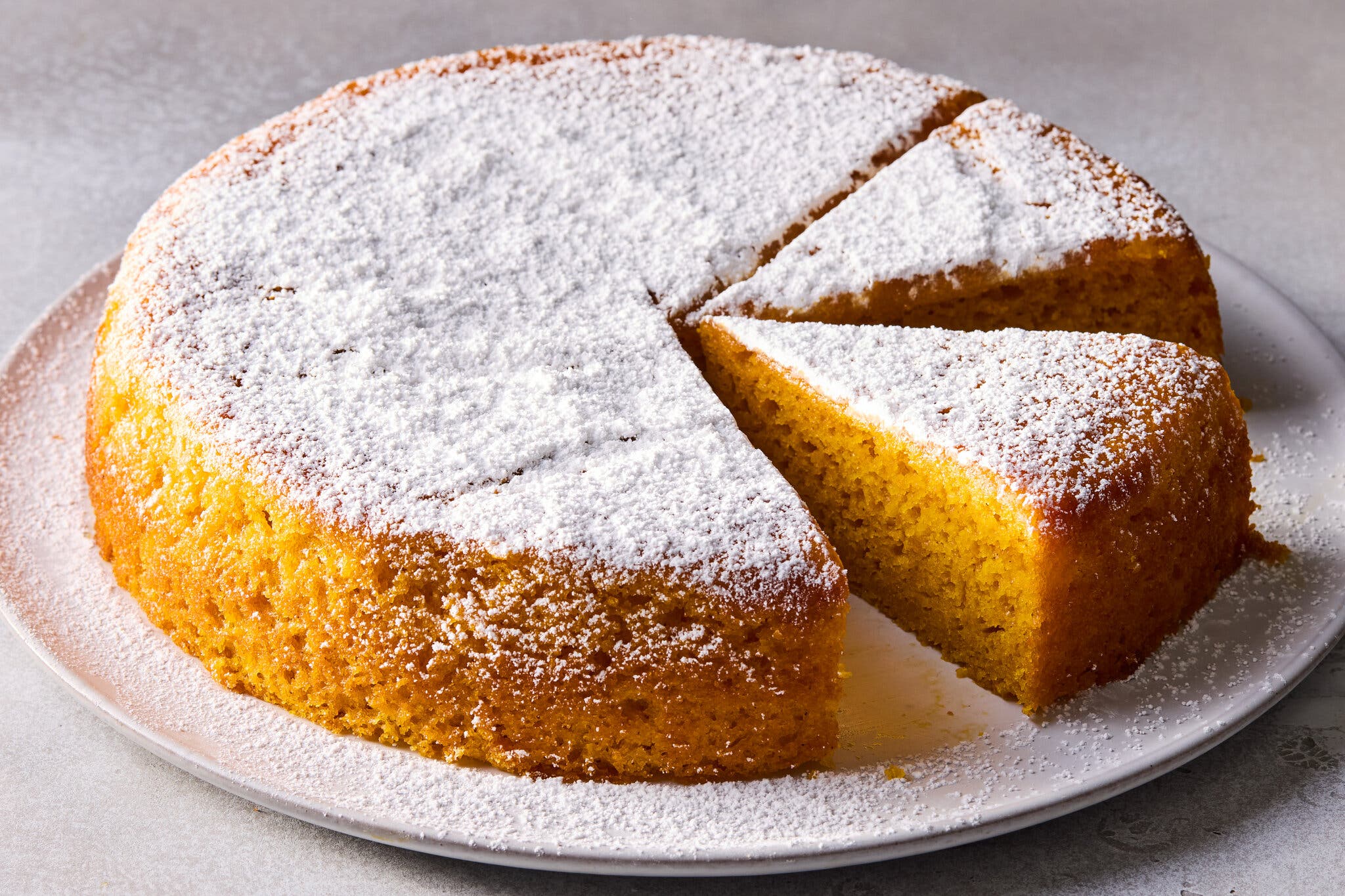 A circular yellow cake dusted with powdered sugar and a slice cut out of it.