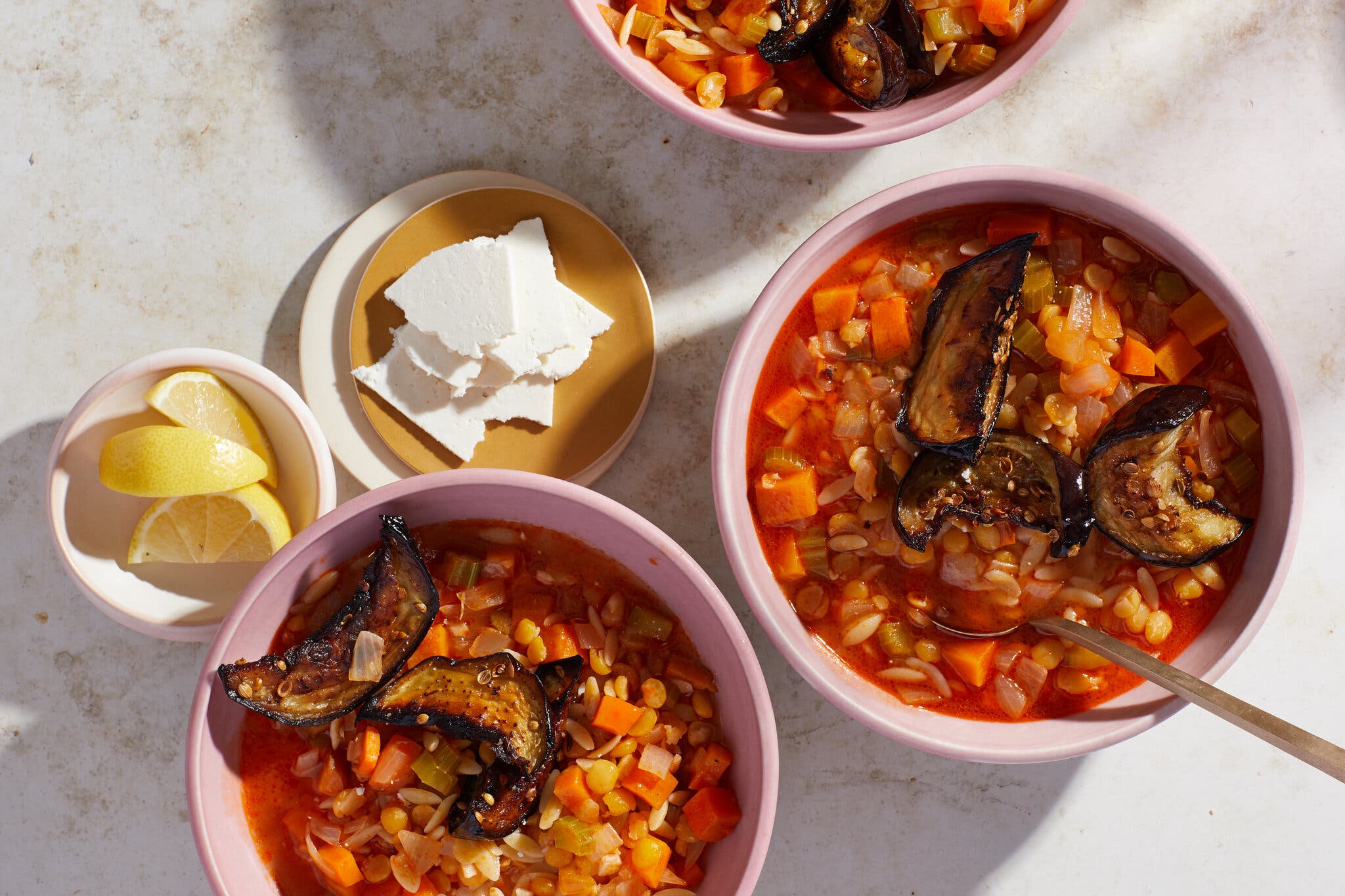 An overhead image of multiple pink bowls filled with soup and topped with roasted eggplant.