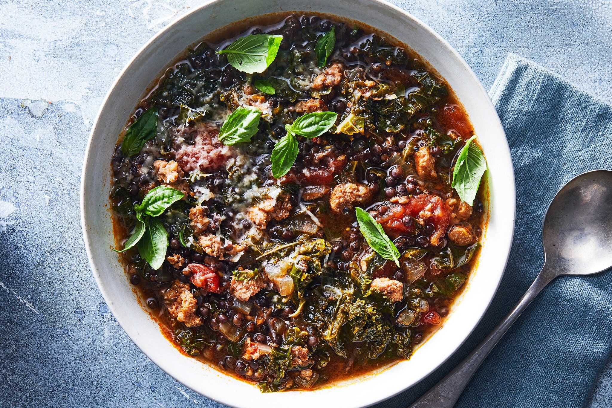An overhead image of lentil soup on a blue tablecloth topped with herbs.