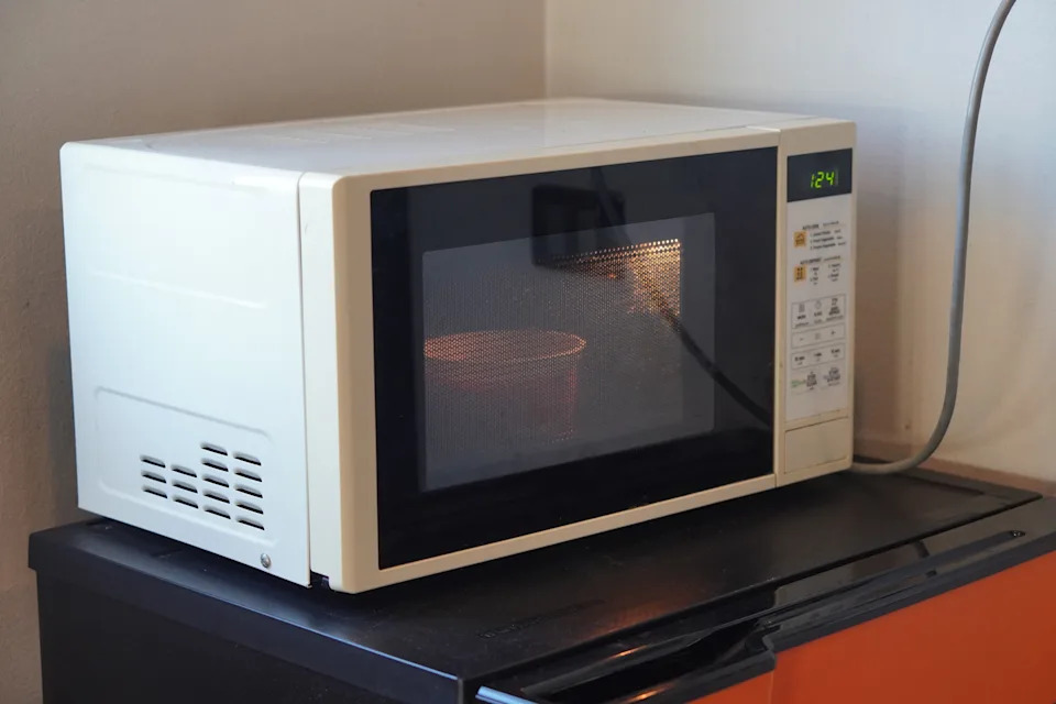 Microwave on a countertop with a cup inside, door closed, displaying the time 12:24 on its screen