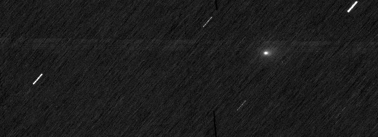 A black space background with white streaks and a single fuzzy white dot. The streaks are stars and the dot is comet 3I/ATLAS.
