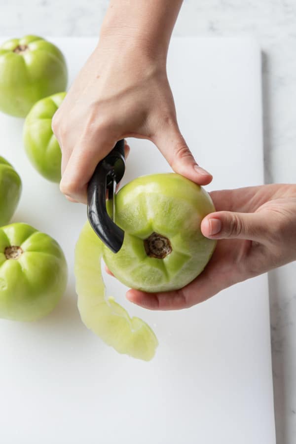 Peeling a green tomato with a vegetable peeler.
