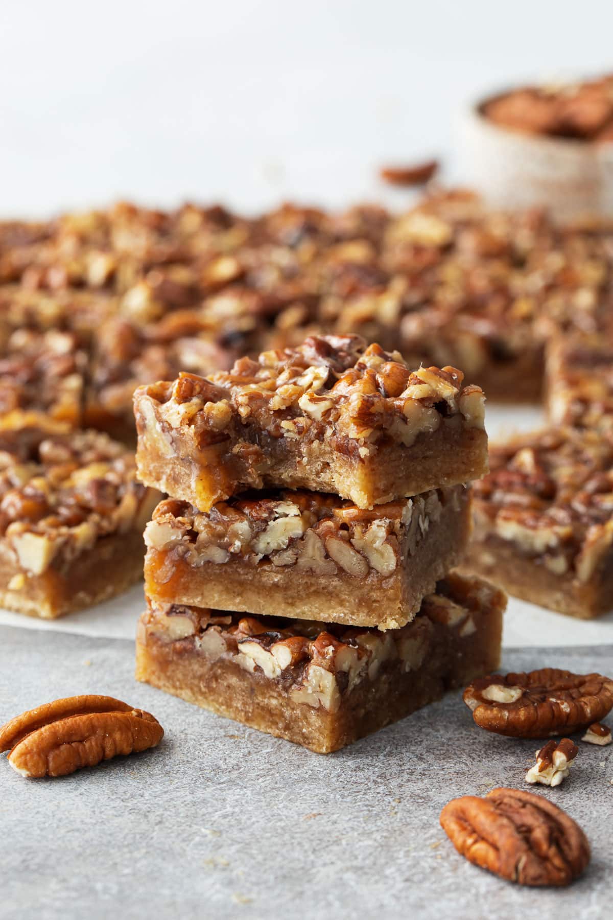 Stack of Pecan Pie Shortbread Cookie Bars, one with a bite taken out of it to show the texture and layers.