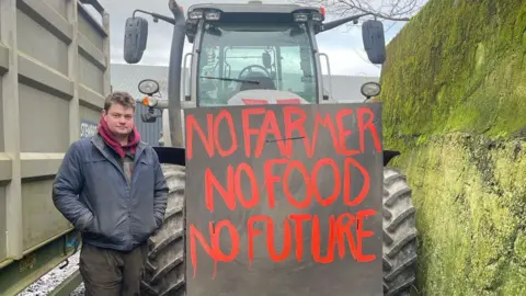 A man stands in front of a tractor and next to a sign which reads: "No farmer no food no future"
