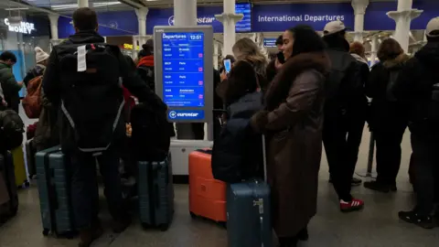 Reuters Passengers wait with luggage next to a departure board showing cancelled trains