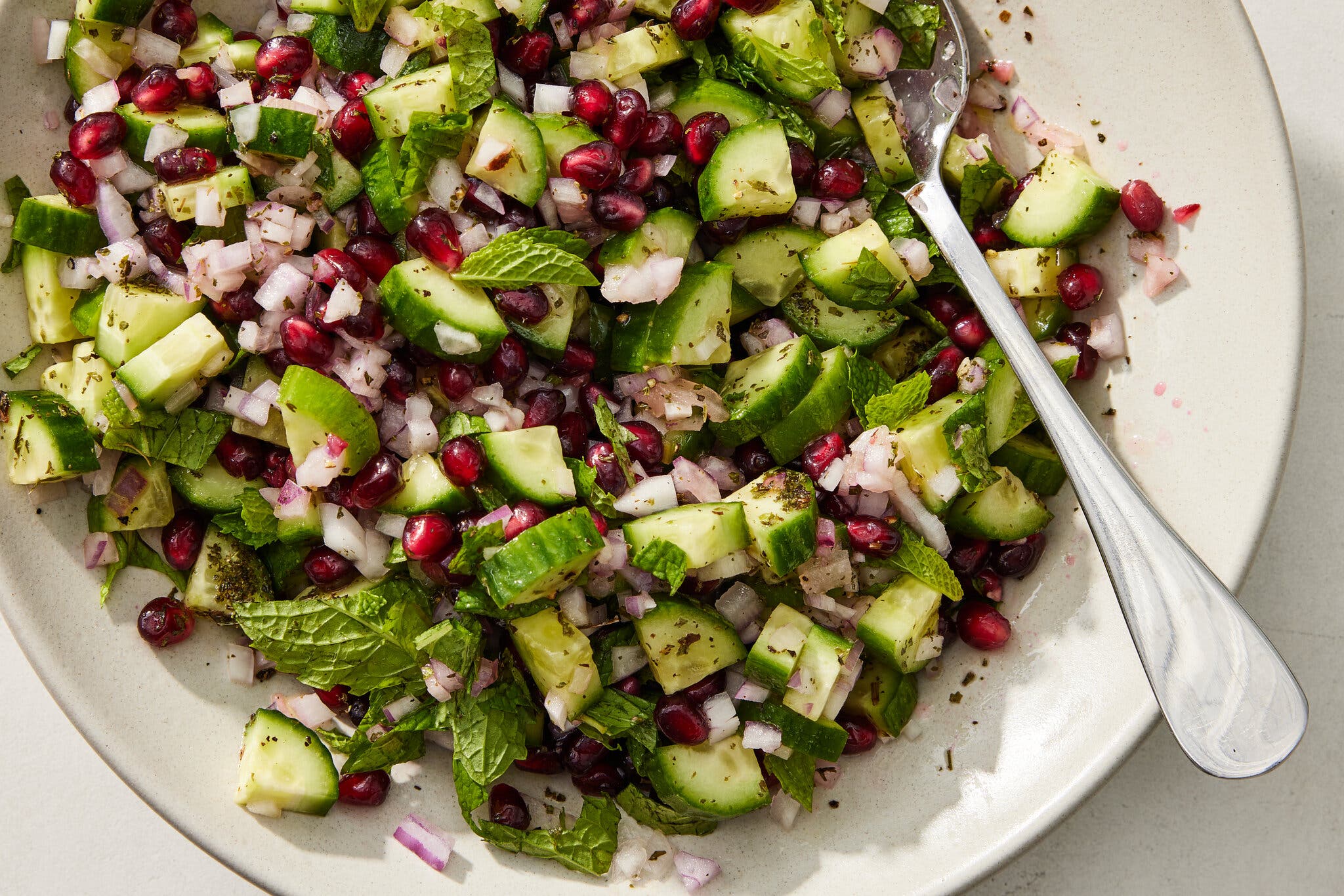 An overhead image of a bowl filled with cucumbers, pomegranate and shallots.